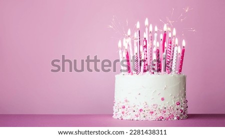 Pink birthday cake with many pink birthday candles and sparklers against a pink background with copy space