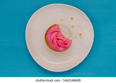 Pink Bitten Cupcake On A Plate Isolated On Blue Background. Delicious Cake. Top View.
