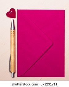 Pink blank envelope little heart and pen on wooden surface.  Valentine day card, love or wedding greeting concept.