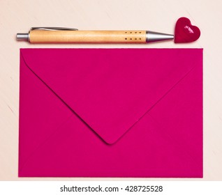 Pink blank envelope little heart and pen on wooden surface. Valentine day card, love or wedding greeting concept.