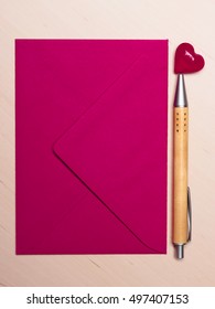 Pink blank envelope little heart and pen on wooden surface. Valentine day card, love or wedding greeting concept.