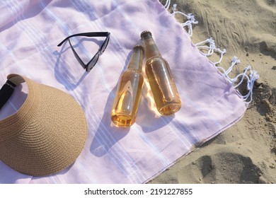 Pink Blanket With Stylish Visor Cap, Sunglasses And Bottles Of Beer On Sandy Beach, Above View
