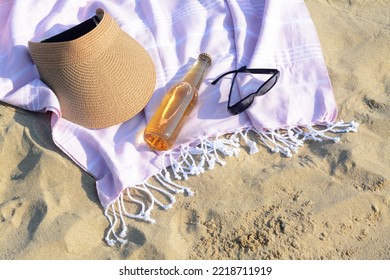 Pink Blanket With Stylish Visor Cap, Sunglasses And Bottle Of Beer On Sandy Beach, Above View