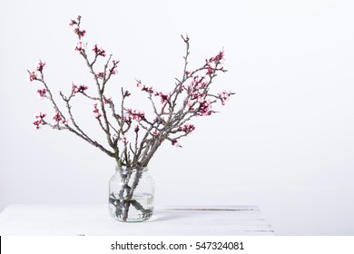 pink blossoming peach flower branches at simple old glass jar on white wooden table - Powered by Shutterstock