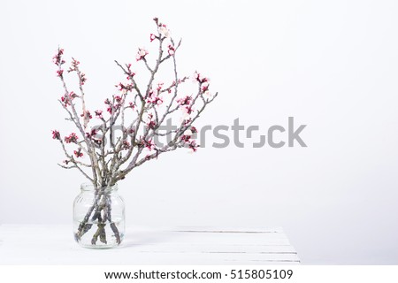 pink blossoming peach flower branches at simple old glass jar on white wooden table