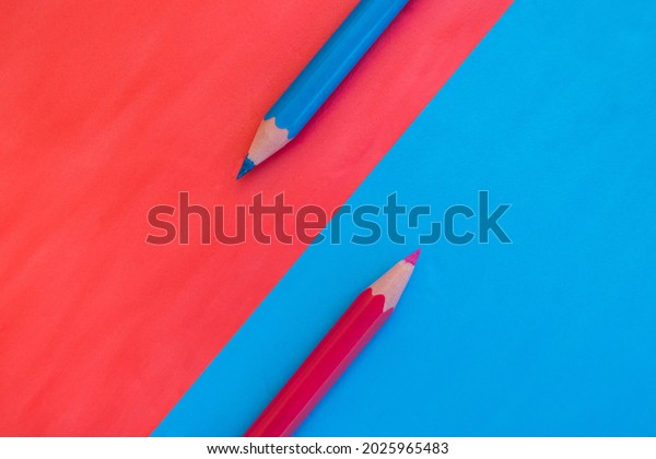 Pink and blue background divided\
diagonally with two matching colored pencils placed on opposite\
colors. Top down view flat lay with empty space for\
text