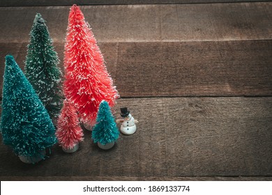 Pink, Blue, And Green Bottlebrush Christmas Trees With A Traditional Frosty The Snowman (complete With Top Hat, Coal, And Carrot Nose) On Worn Wood.