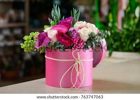 Pink box with flower bouquet on florist's table. Wonderful composition of violet, red, white blossoms with greenery is a perfect present for girlfriend's birthday.