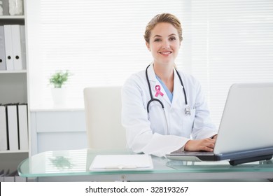 Pink breast cancer awareness ribbon against doctor smiling as she types
