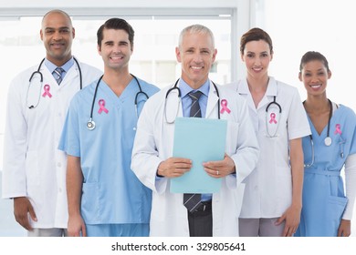 Pink breast cancer awareness ribbon against team of smiling doctors looking at camera