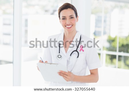 Pink breast cancer awareness ribbon against beautiful doctor reading files