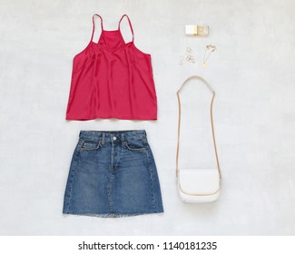 Pink cami top, blue denim mini skirt, small white cross body bag with chain strap, gold jewelry on grey background. Overhead view of woman's casual outfits. Flat lay, top view. Trendy summer look. - Shutterstock ID 1140181235