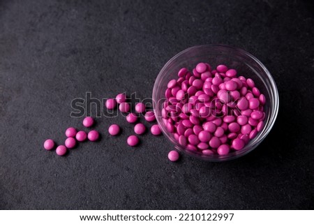 Pink candy coated chocolate button sprinkles in a bowl on dark slate - MMs, Smarties, sprinkles