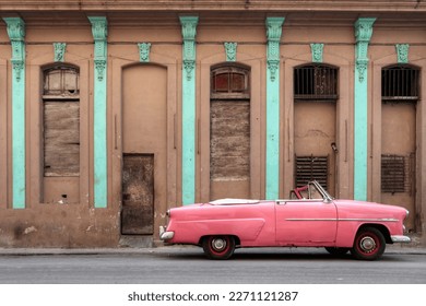 A pink car in Havana, Cuba park in front of an brown facade  - Powered by Shutterstock - Get 15% off with code: PIKWIZARD15