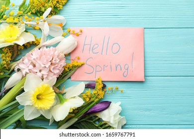 Pink card with words HELLO SPRING and fresh flowers on light blue wooden table, flat lay