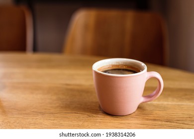 A pink ceramic cup of hot black coffee on a wooden table, cafe, copy space
