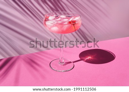 Pink champagne with ice on the table with sun shadows. On a pink background with palm leaves, front view.