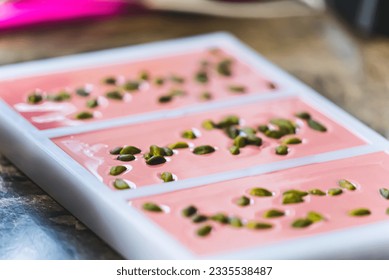 Pink chocolate bars in moulds. Ruby chocolate production process. Modern chocoat with pistachios. Chocolate moulds isolated on brown kitchen counter. High quality photo