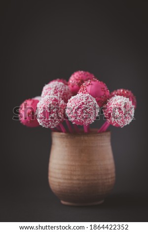 Pink chocolate cake pops in the rustic brown cup on the vintage dark background. Bisquit cake pops sprinkled with coconut flakes. St. Valentine's Day