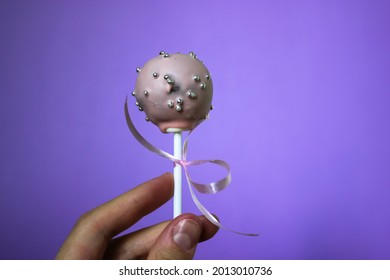 Pink chocolate cake pops with strawberry flavour on a purple background. A round cake on a stick decorated with ribbon and confectionery sprinkles of silver beads. A sweet treat. World Chocolate Day. - Powered by Shutterstock