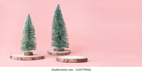 Pink Christmas background.Christmas tree on wood log trunks slice with gift box on pastel pink studio backdrop.Holiday festive celebration greeting card with banner copy space for display of design