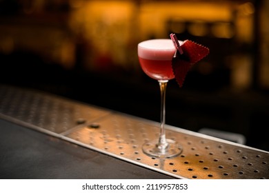 Pink Cocktail Decorated With Fruit Marshmallow Standing On Metal Bar Counter. Shelves With Bottles Of Alcohol In Background.