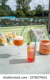 Pink Cocktails Served Outside On A Sunny Terrace With A Green Couch And A Blue Swimming Pool In The Background, No People