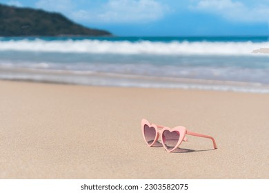 Pink color sunglasses in heart shape on sandy beach at tropical seaside on warm sunny day. Summer vacation concept. Copy space, closeup