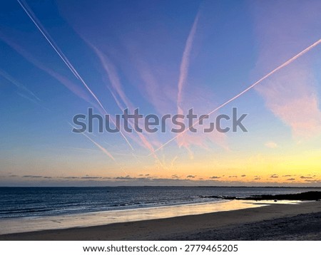 Pink comms trails over a beach at sunset with calm sea
