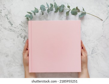 Pink Cover Book With Copy Space On A Marble Background And Eucalyptus Twig. Woman Holding Pink Book Album