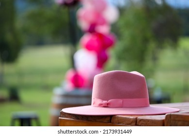 A pink cowgirl hat sitting on a table outside with balloons in the background. 
