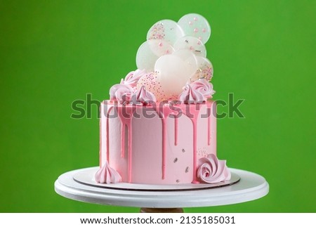 Pink cream cheese cake with chocolate chip gouges decorated with meringues and isomalt lollipops. Beautiful delicious birthday cake on the green background. Picture for a menu