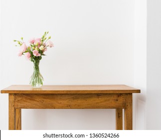 Pink and cream lisianthus flowers in glass vase on oak wooden sidetable against white wall