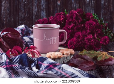 A pink cup of coffee, burgundy asters, autumn grape leaves, cookies and a scarf. Happy autumn mood. Autumn composition on a dark background.
