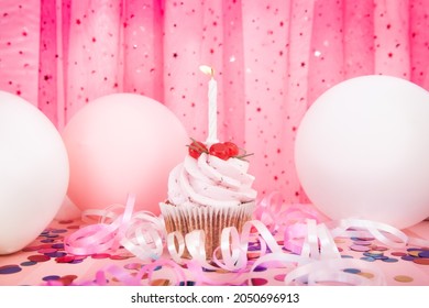 Pink cupcake and white one candle on colorful background with air balloons, happy birthday and anniversary concept