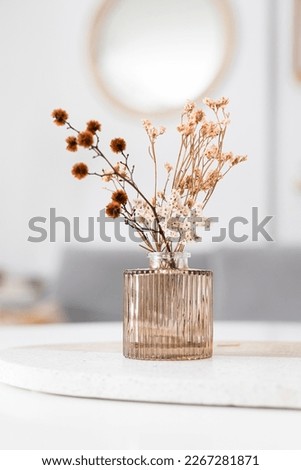A pink design glass vase with dried wild flowers inside over a granite board.