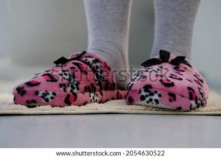pink domestic slipper with black bow on women's legs, feet on a light plush rug, concept of comfortable shoes for rest, relax and life, taking care of healthy feet, sweet home