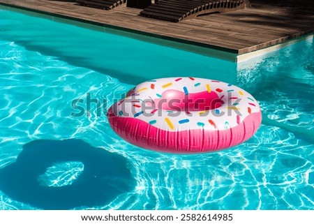 Pink donut inflatable float in turquoise swimming pool with wooden deck and sunny highlights