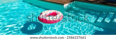 Pink donut inflatable float in turquoise swimming pool with shadow, wooden deck, and submerged steps