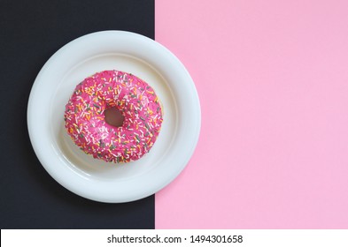 Pink donut in plate with colorful sprinkles on two-tone background, top view with copy space - Powered by Shutterstock