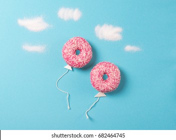 Pink donuts on blue background, creative food minimalism, donut in a shape of balloon in the sky with clouds made of sugar, top view - Powered by Shutterstock