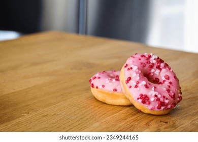 Pink donuts on a wooden table. Donuts with strawberry glaze, white and pink sprinkles.