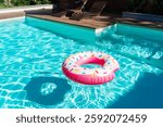 Pink donut-shaped inflatable float in turquoise swimming pool with wooden deck and sunny reflections