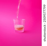 Pink drink being poured into a glass with a pink background