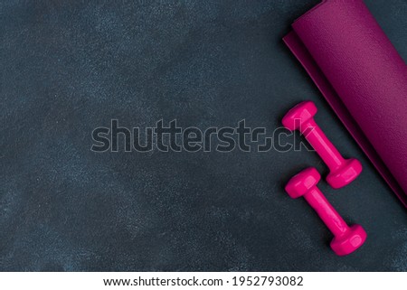 Pink dumbbells, purple yogamat. Black cement background. Empty copy space.