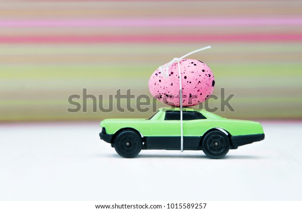 \
Pink Easter egg on the roof of\
a green toy car. Delivery of products to Easter. Easter\
concept.
