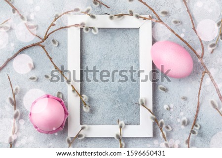 Pink easter eggs on gray table with willow twigs and white wooden frame - easter composition with copy space, flatlay