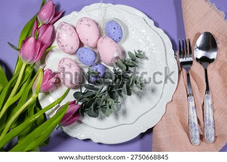 pink Easter eggs on a serving plate. Bouquet of pink tulips on a lilac background, Easter holiday