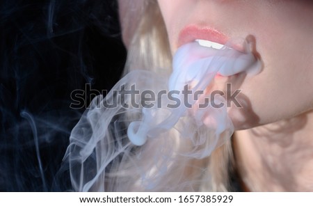 Pink female lips and cigarette smoke. Blonde woman exhales cigarette smoke.