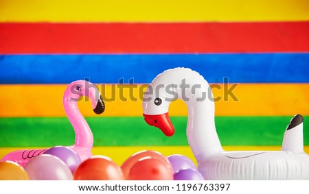 Pink flamingo and white goose balloons along with normal balloons in front of multicolored striped background